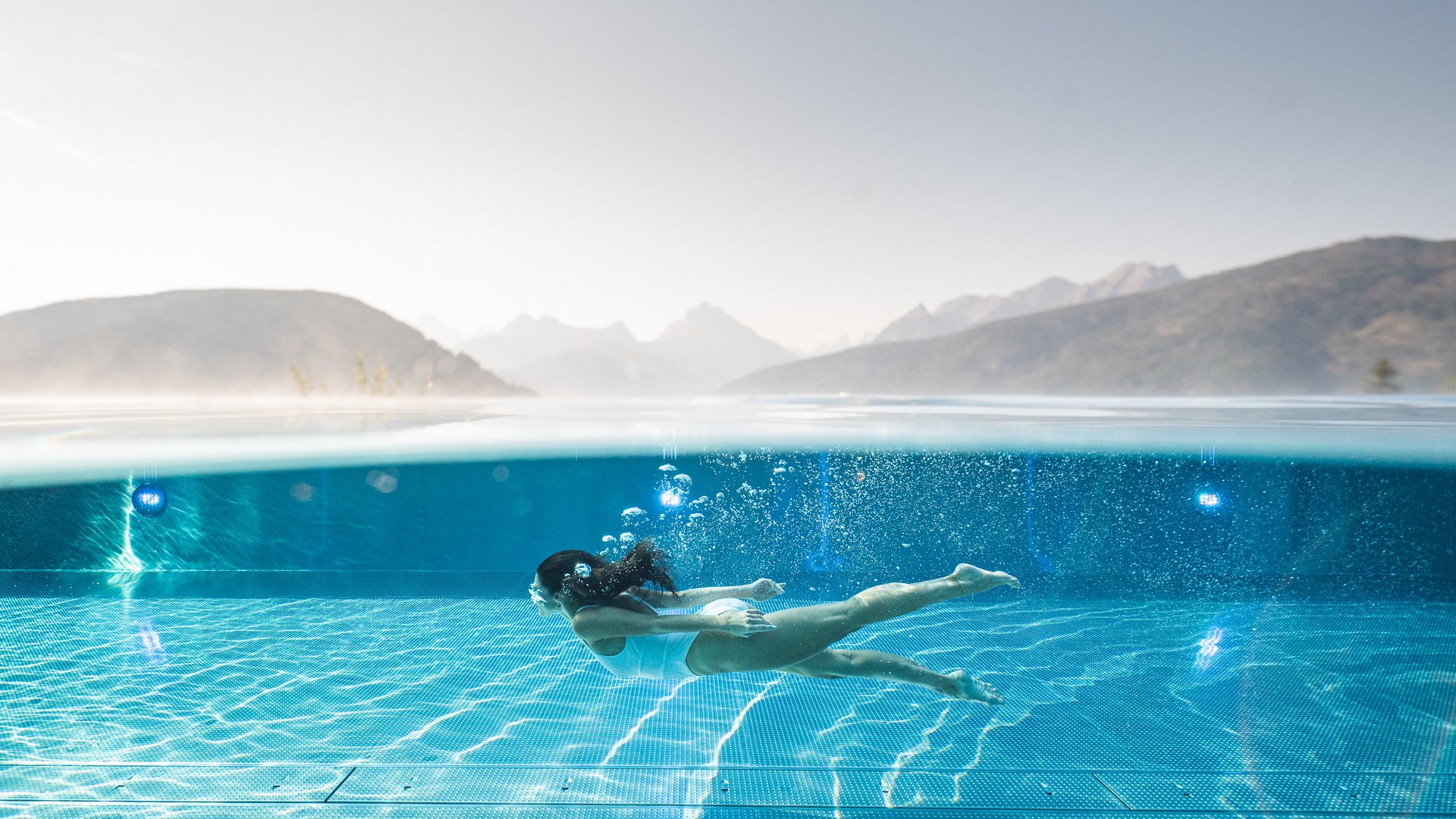 Your hotel in Val Pusteria/Pustertal with pool oasis Woman swimming underwater in a pool with mountain view