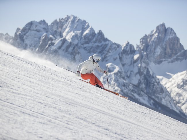 5-Sterne-Sporthotel in Südtirol gesucht? Skifahrer in weißer Jacke und roter Hose fährt auf verschneiter Piste vor Bergkulisse