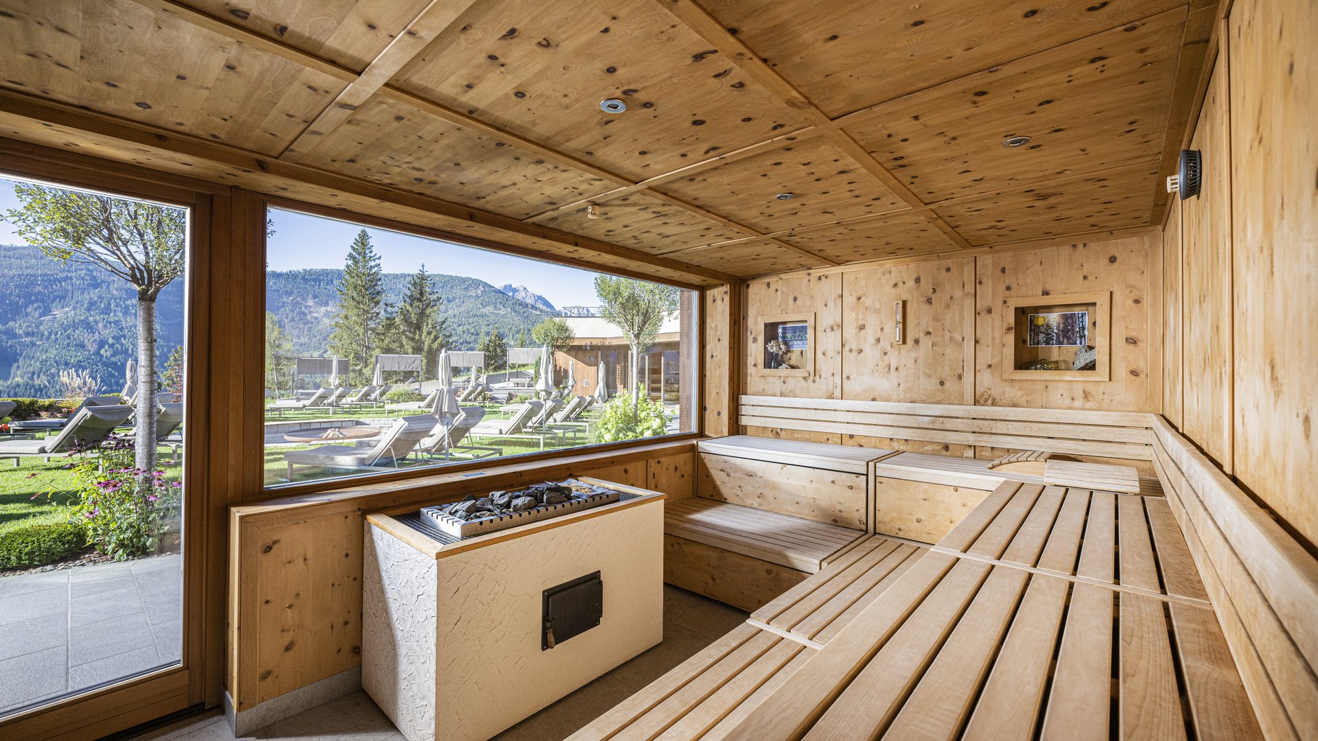 Hotel con sauna in Alto Adige:l’Alpen Tesitin Sauna in legno luminosa con vista su sdraio e paesaggio montano esterno