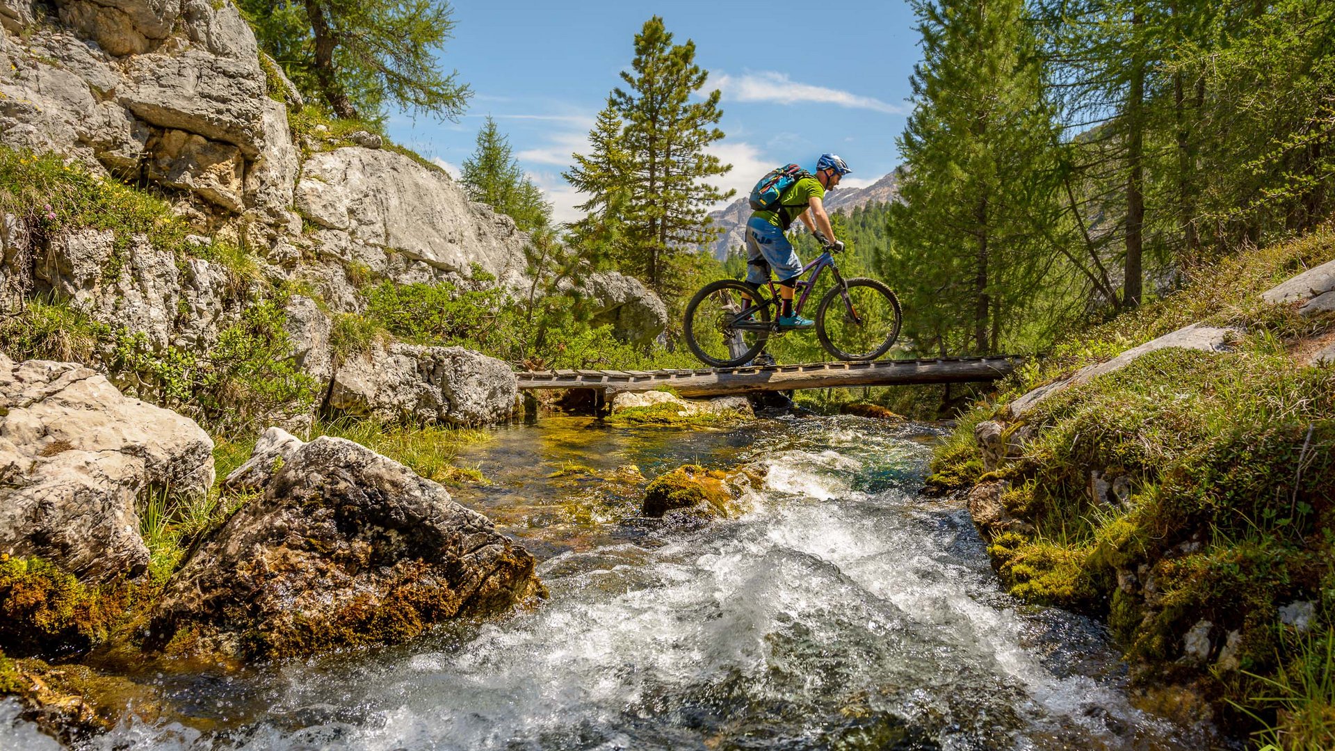 Ciclista attraversa ponte di legno su ruscello in paesaggio montano boscoso