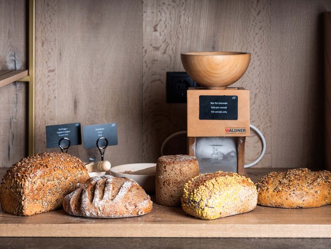 Varie tipologie di pane davanti a un mulino per cereali in una cucina di legno