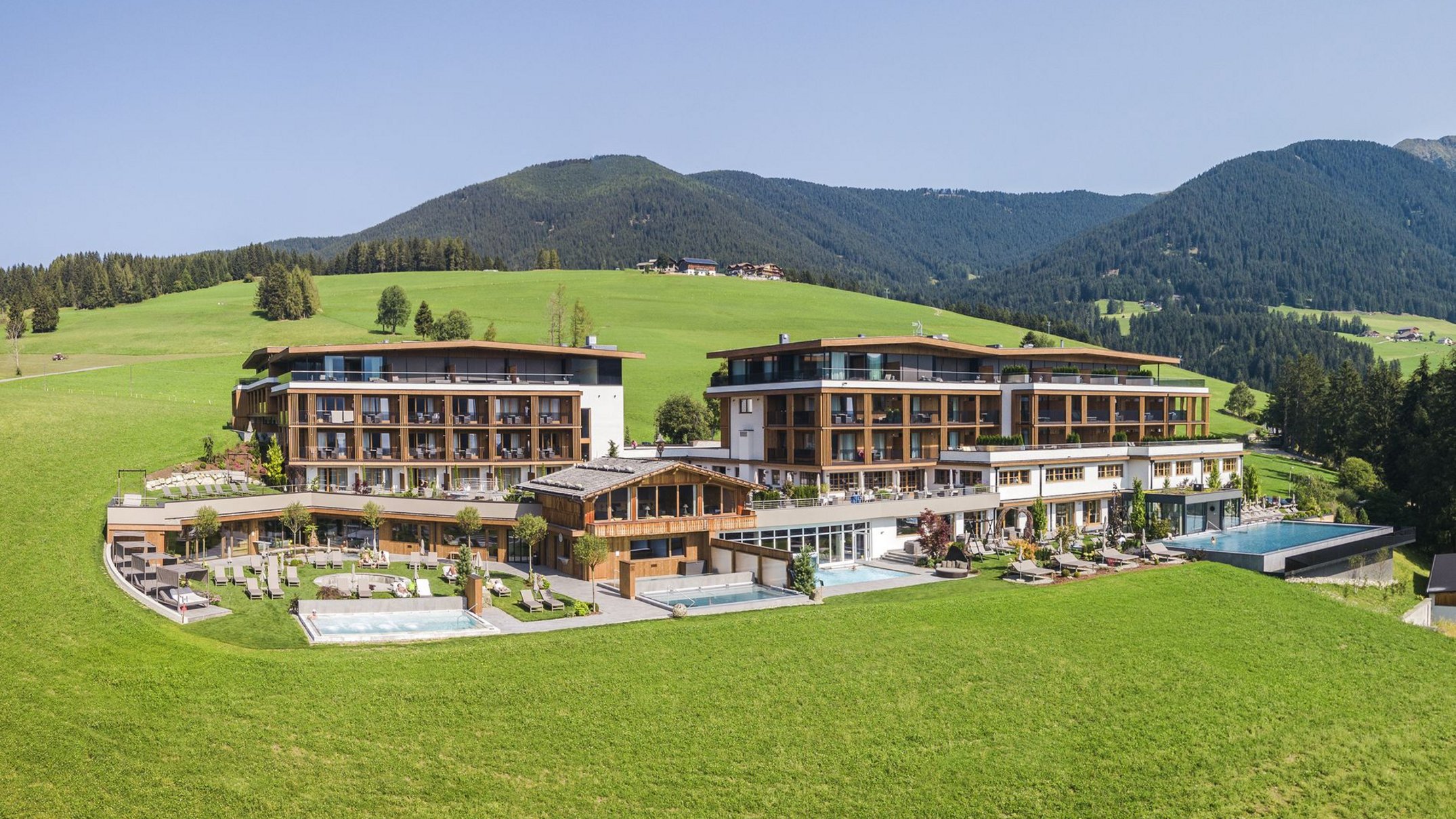 Alpen Tesitin: una storia da raccontare Hotel moderno in paesaggio alpino verde con piscina esterna e terrazza panoramica
