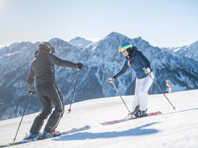 Sciare in Val Pusteria in vacanza all’Alpen Tesitin Due sciatori su una pista innevata con montagne sullo sfondo