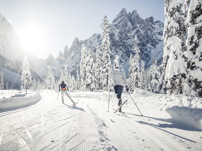 Langlaufen im Pustertal Zwei Langläufer auf einer sonnigen Schnee-Piste in verschneiter Berglandschaft