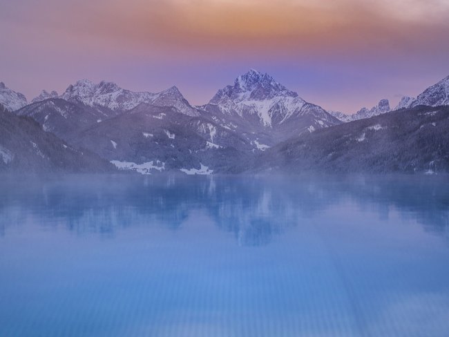 Verschneite Berge spiegeln sich bei Abenddämmerung in einem ruhigen See