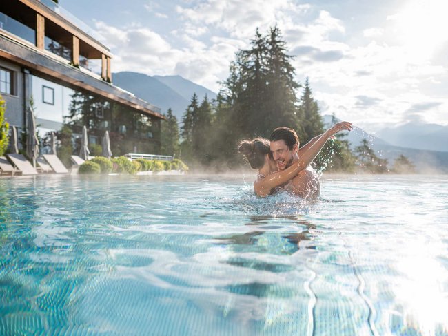 Paar umarmt sich lachend im Pool mit Bergblick