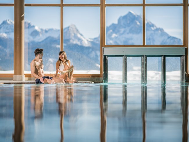 Paar entspannt im Hallenbad mit Bergblick durch große Fenster