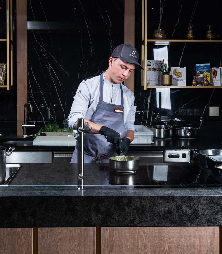Alpen Tesitin: Ihr Gourmethotel in Südtirol Koch bereitet Essen in moderner Küche mit schwarzer Marmorwand zu