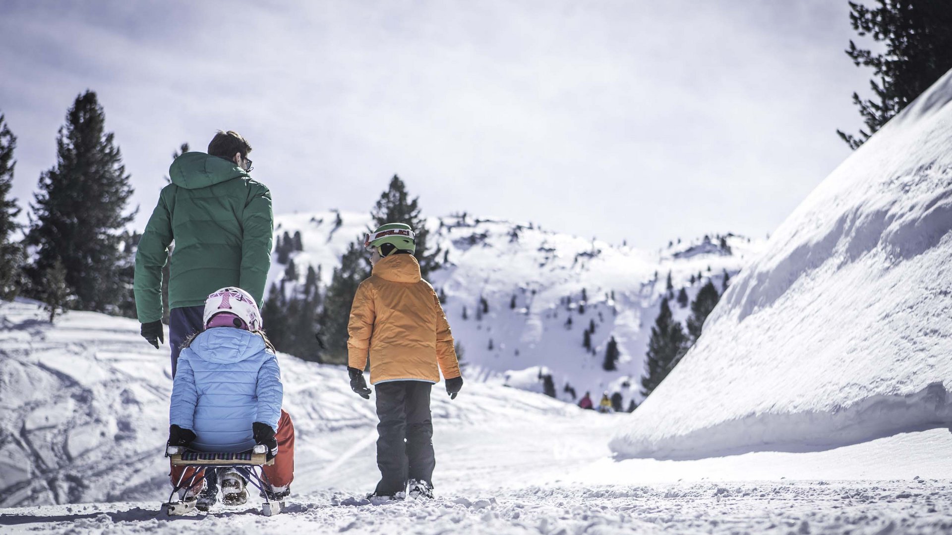 Padre con due bambini che fanno slittino in montagna innevata
