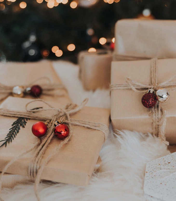 Weihnachtsgeschenke in braunem Papier mit roten und silbernen Kugeln unter Baum