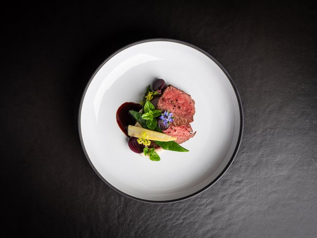 Anrichteweise von rosa gebratenem Fleisch mit Babymais, Blättern und Sauce