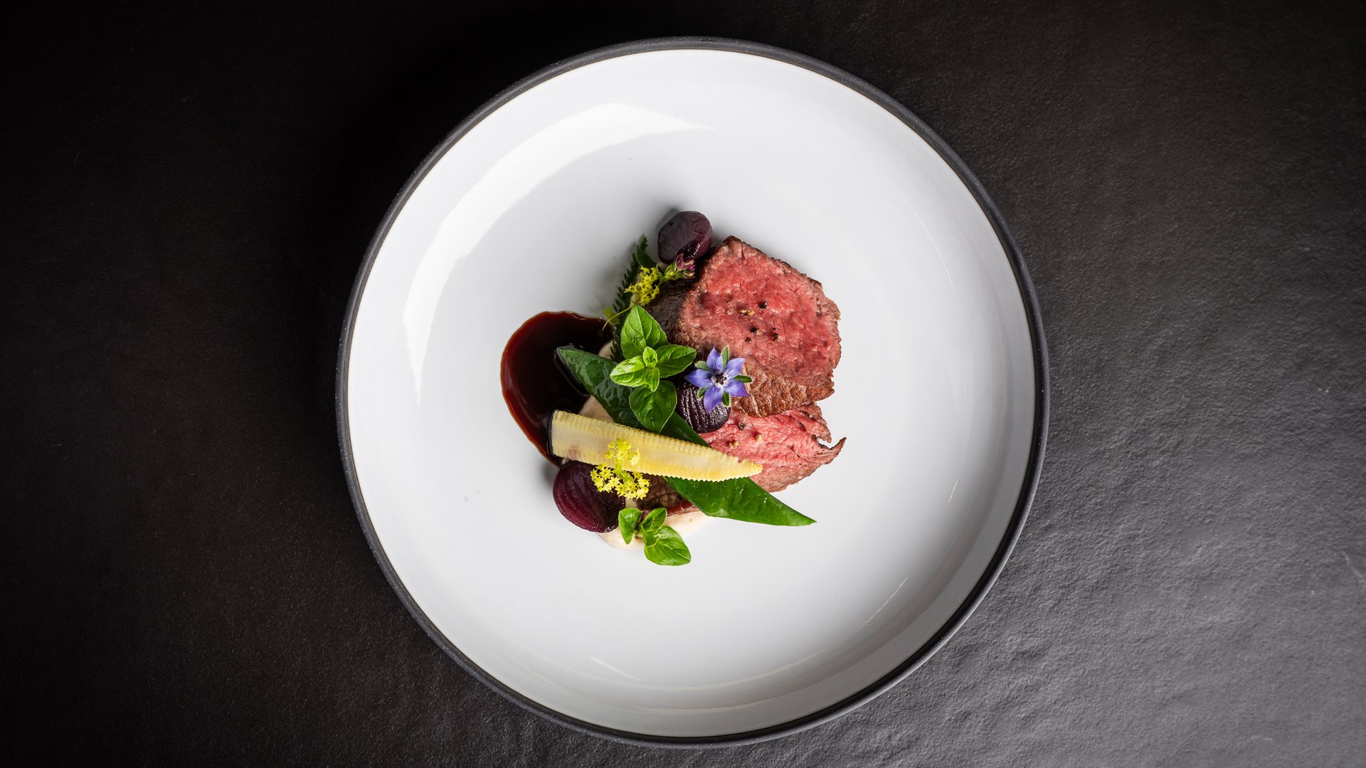 Anrichteweise von rosa gebratenem Fleisch mit Babymais, Blättern und Sauce