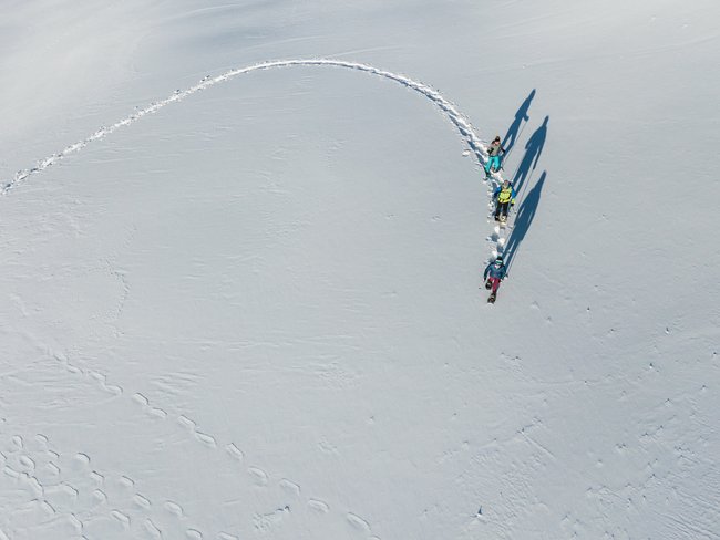 Three people hiking on snow-covered field with long shadows in sunlight