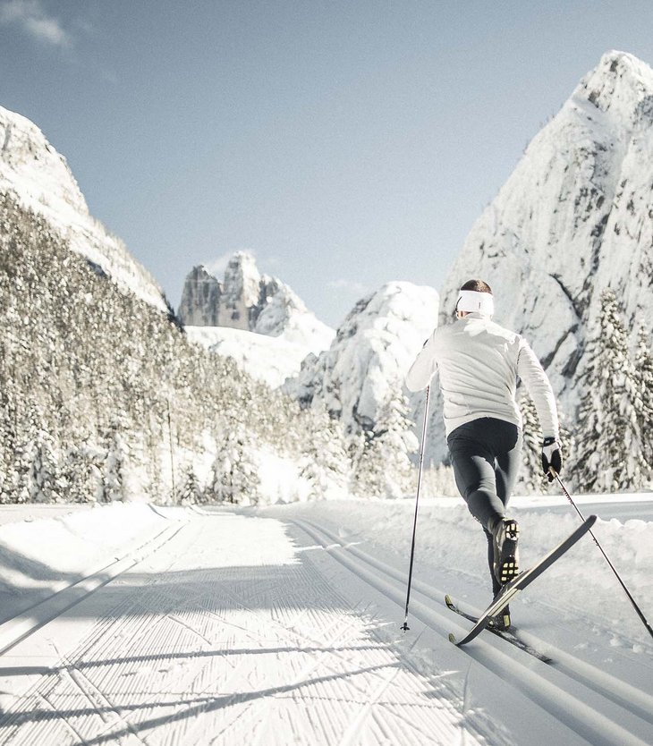 Cross-country skier in white gear on snowy trail with mountain backdrop