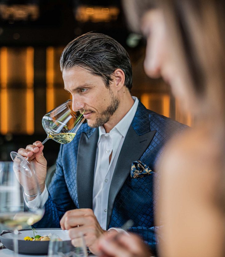 Alpen Tesitin: Ihr Gourmethotel in Südtirol Mann in blauem Anzug riecht Weißwein im eleganten Restaurant