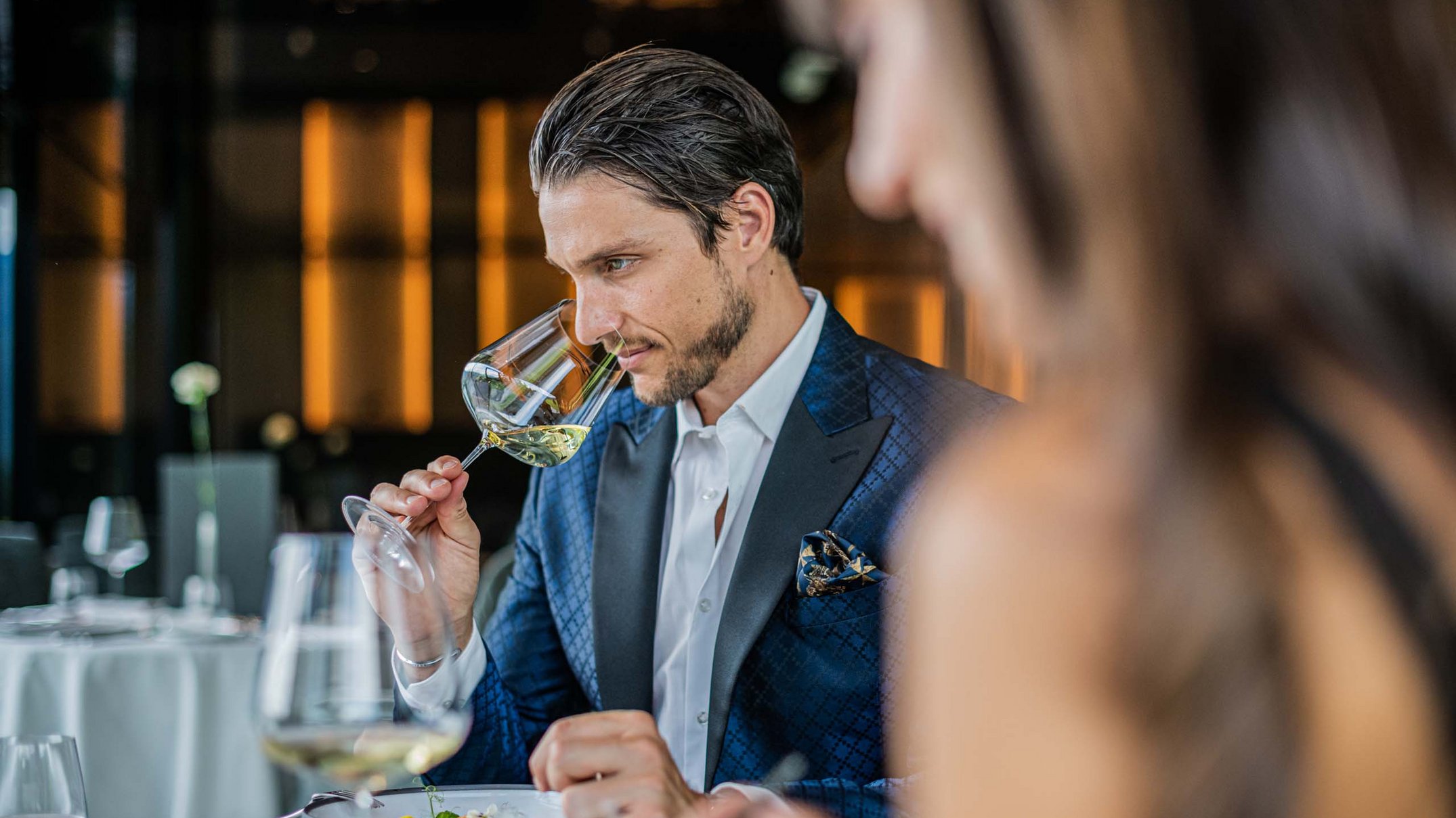 Alpen Tesitin: Ihr Gourmethotel in Südtirol Mann in blauem Anzug riecht Weißwein im eleganten Restaurant