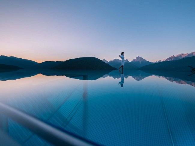 Frau steht am Rand eines Infinity-Pools mit Bergblick bei Sonnenuntergang