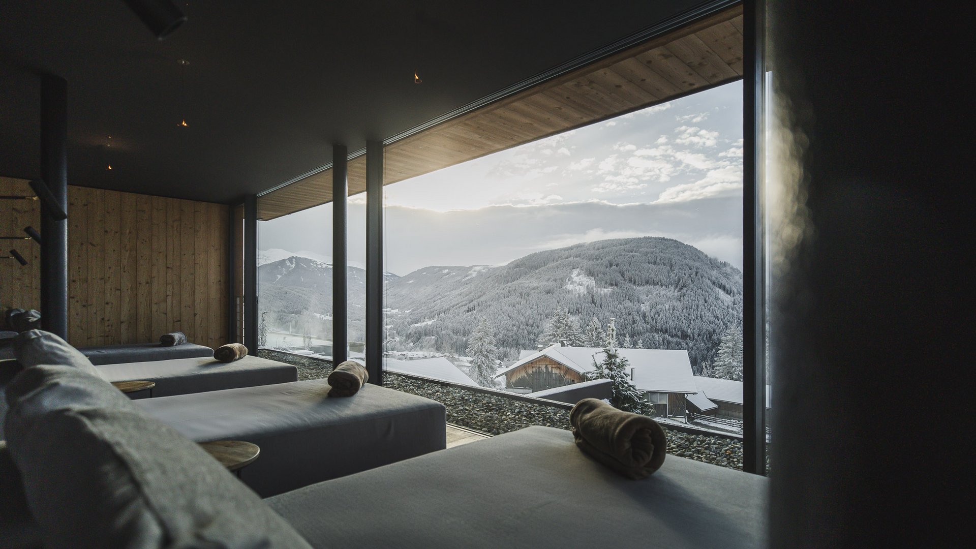 Hotel con sauna in Alto Adige:l’Alpen Tesitin Zona relax con lettini davanti a grandi finestre panoramiche vista montagne innevate