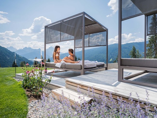 Couple on outdoor canopy bed with mountain view and flowers in foreground