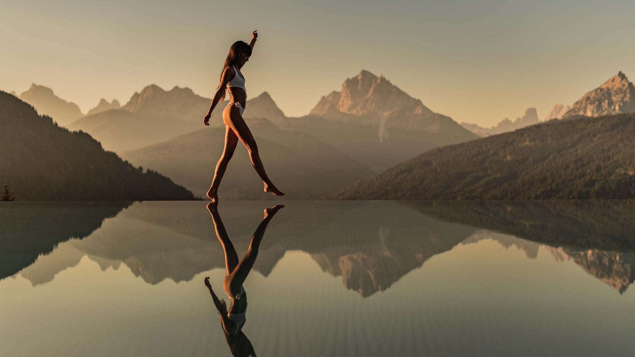 Your 5-star hotel in Val Pusteria/Pustertal: Alpen Tesitin Woman in bikini walking on edge of infinity pool with mountain background