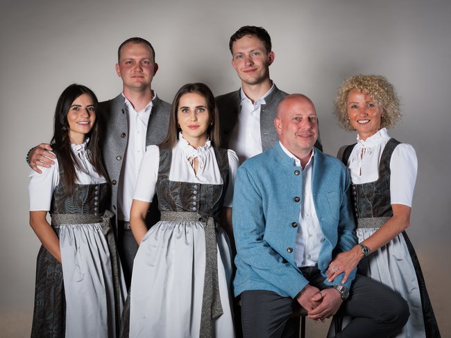 Sechs Personen in traditionellen Trachten posieren vor neutralem Hintergrund