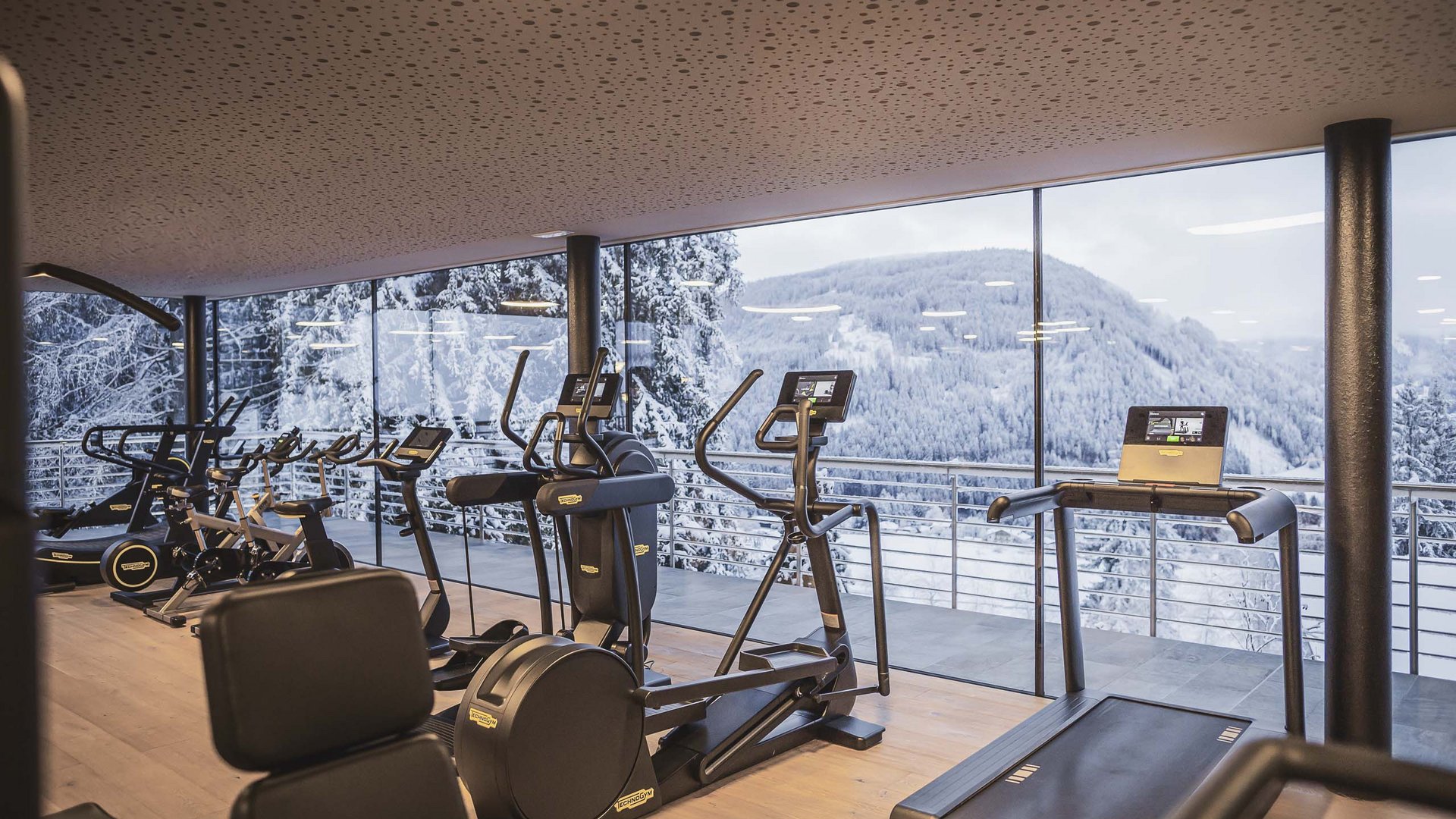 Fitnessraum mit modernen Geräten und Blick auf schneebedeckte Berge