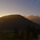 Sonnenaufgang über bewaldetem Hügel und Bergen im Hintergrund