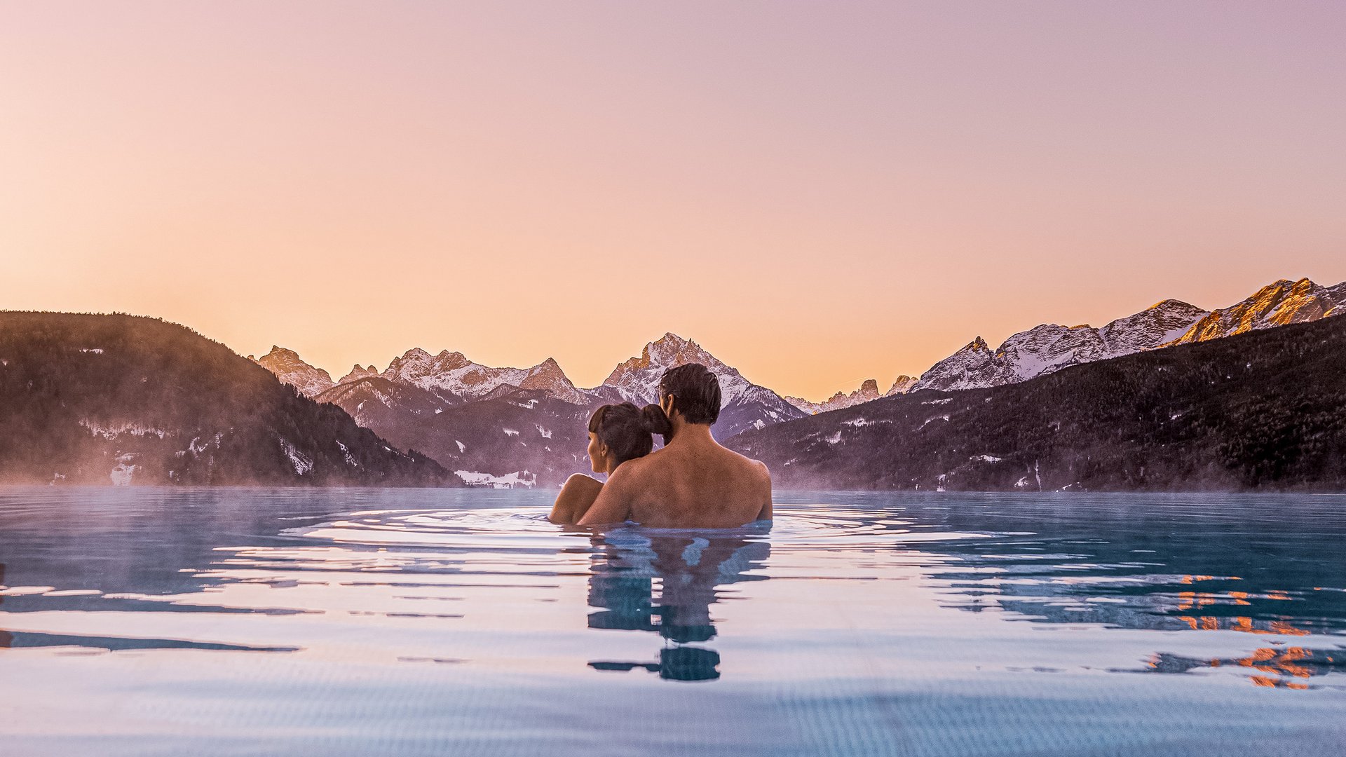 Couple in infinity pool with mountain view at sunset
