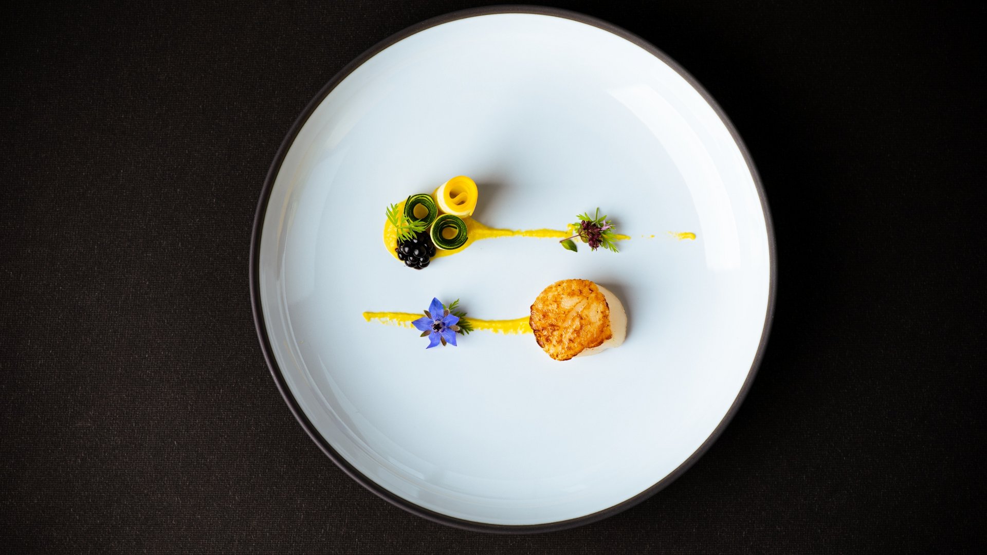 Artistically plated scallop with vegetable rolls and edible flowers on white plate