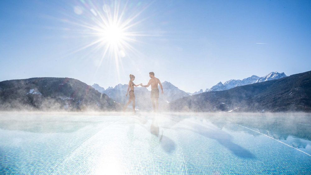Couple in swimwear at steamy pool with mountain view under bright sun