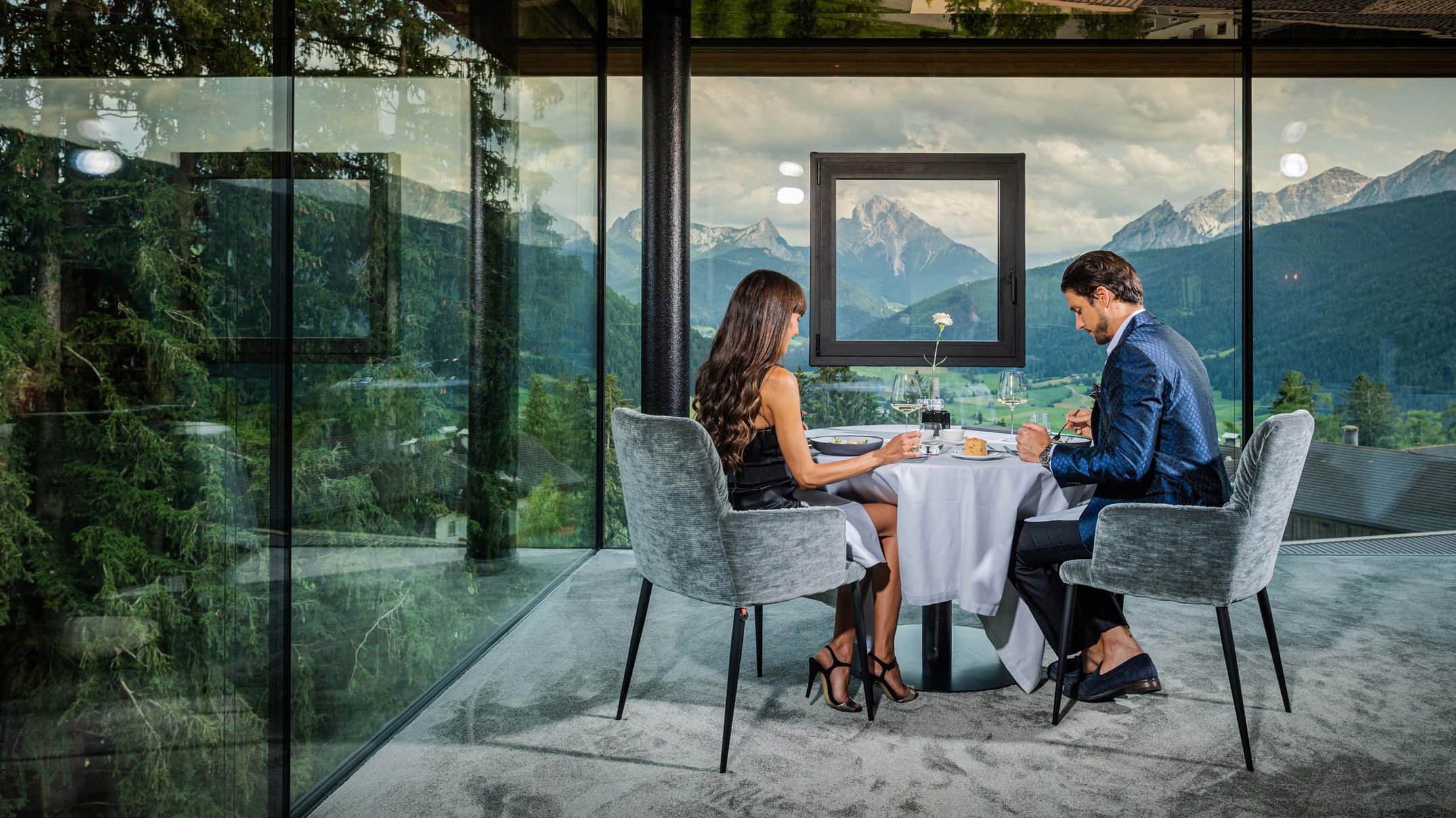 Your 5-star hotel in Val Pusteria/Pustertal: Alpen Tesitin Couple dining in modern glass restaurant with mountain view