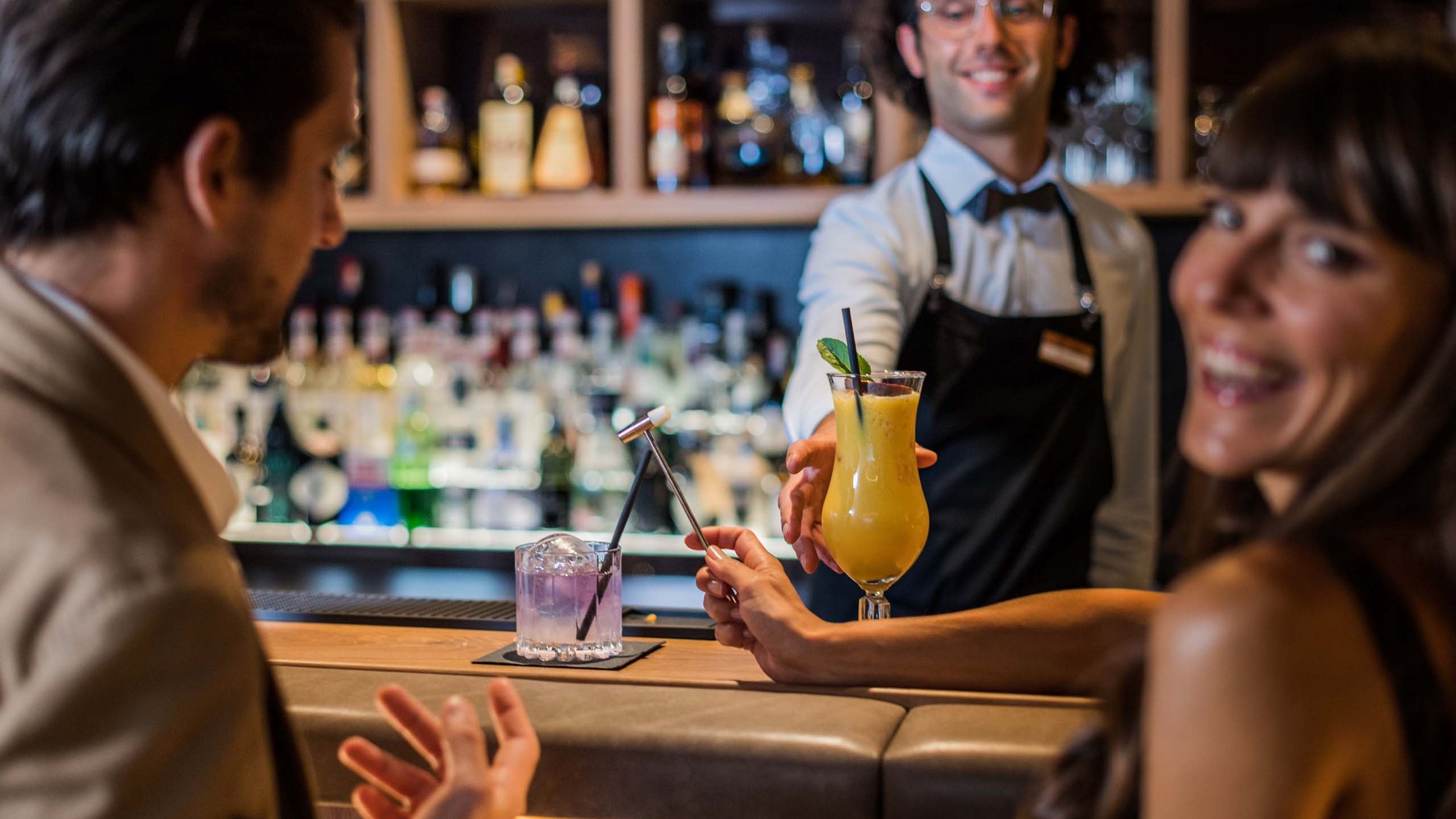 Alpen Tesitin: Ihr Gourmethotel in Südtirol Barkeeper serviert Drinks an ein lächelndes Paar in einer Bar