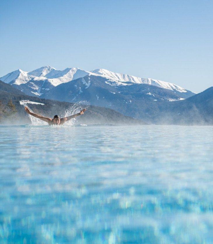 Person swimming in heated pool with snowy mountains in the background