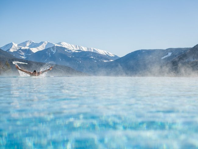 Person schwimmt in beheiztem Pool vor verschneiten Bergen