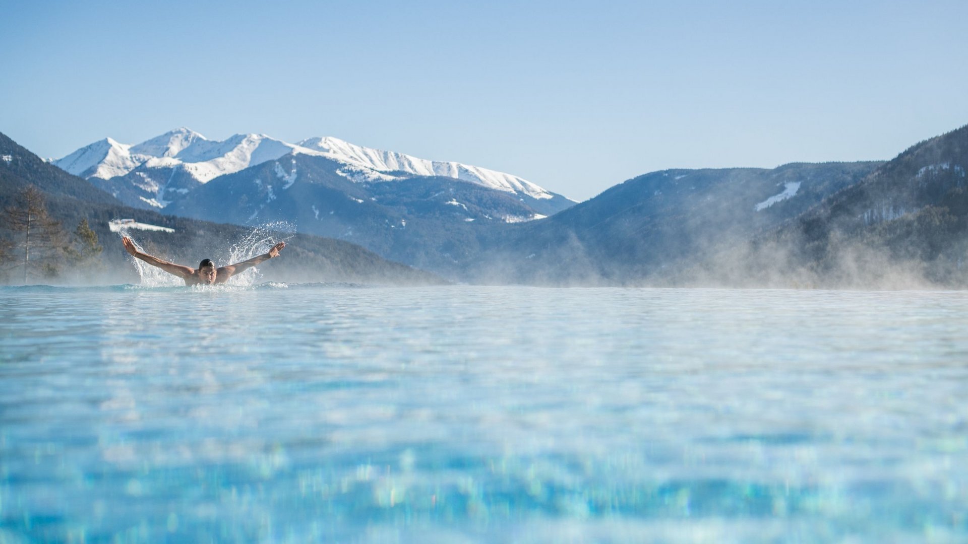 Person swimming in heated pool with snowy mountains in the background