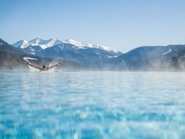 Person schwimmt in beheiztem Pool vor verschneiten Bergen