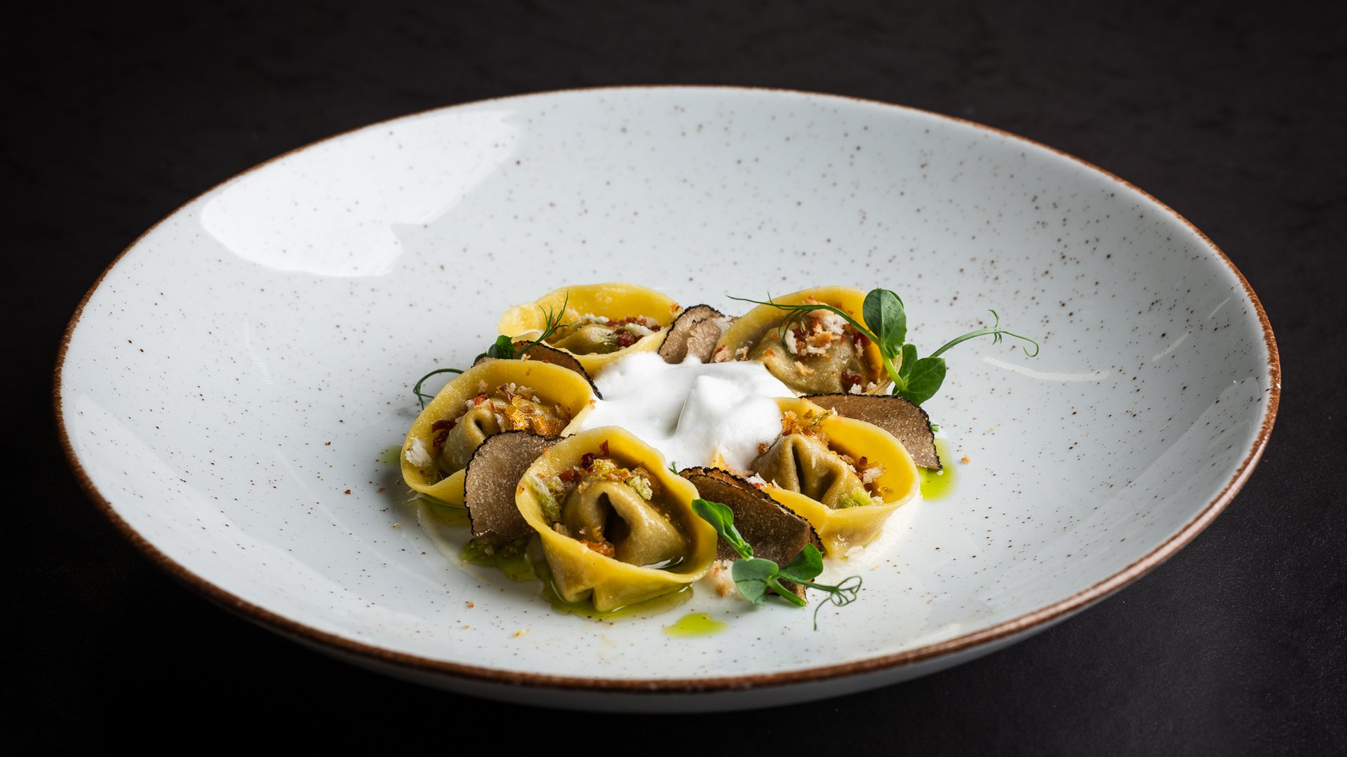 Stuffed tortellini with truffle slices and foam on white plate