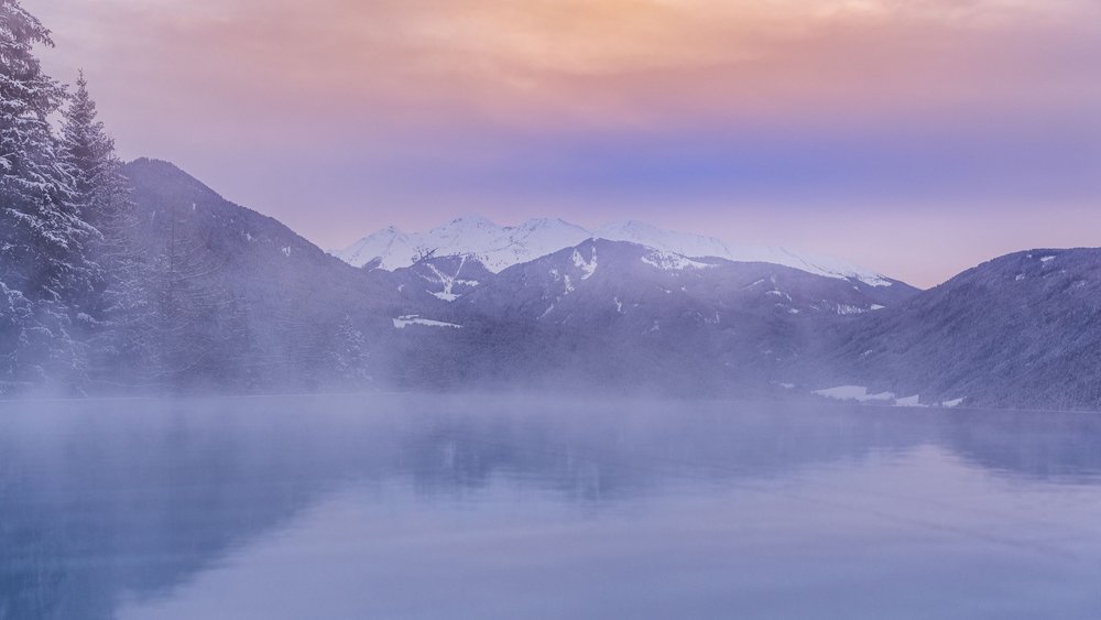 Foggy mountain landscape with snow-covered peaks and calm water