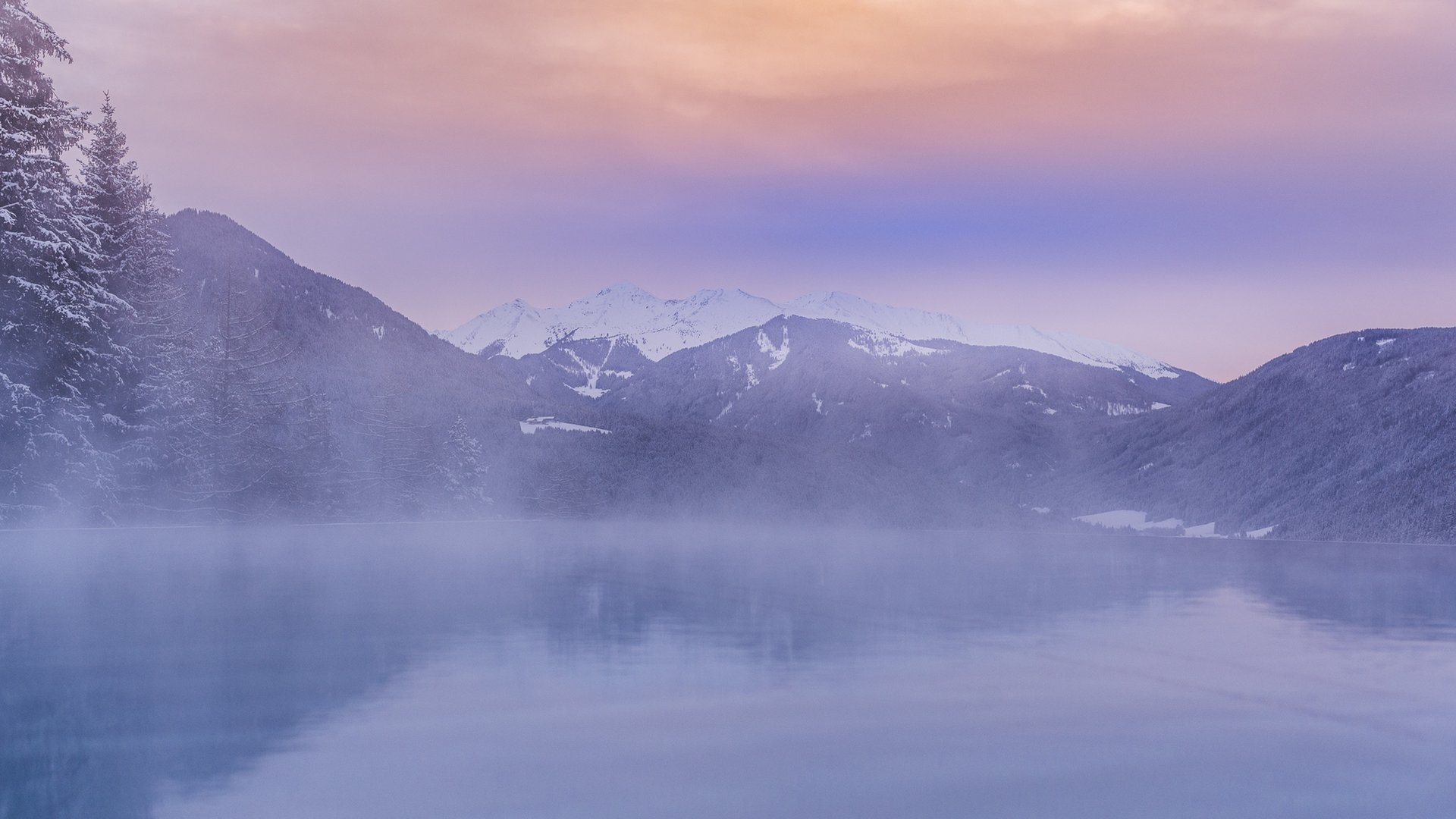 Berglandschaft mit Schnee und nebligem See bei Sonnenuntergang