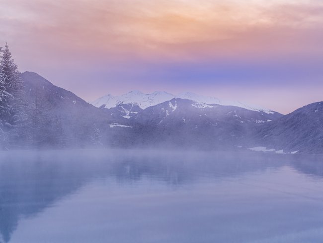Berglandschaft mit Schnee und nebligem See bei Sonnenuntergang