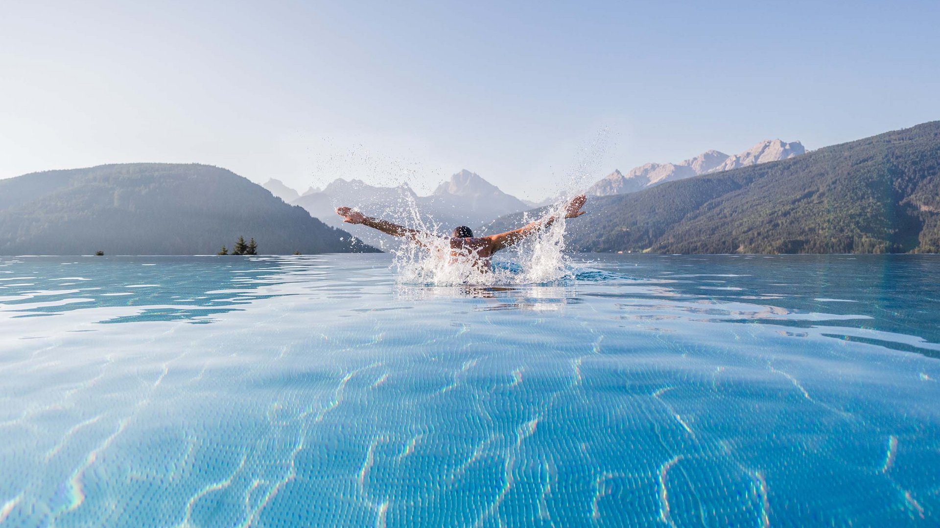 Mann schwimmt im Infinity Pool mit Bergblick an klaren Tag