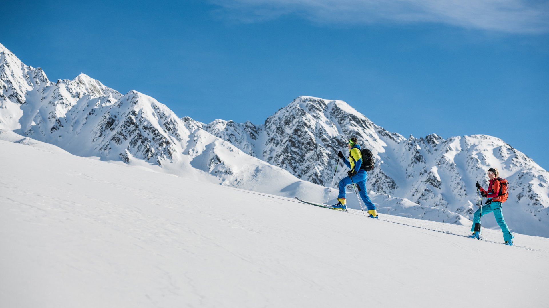 Zwei Skitourengeher steigen bei Sonnenschein einen schneebedeckten Hang hinauf