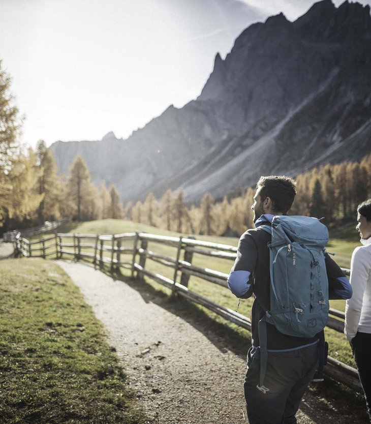 Due escursionisti su un sentiero accanto a una recinzione di legno in paesaggio montano autunnale