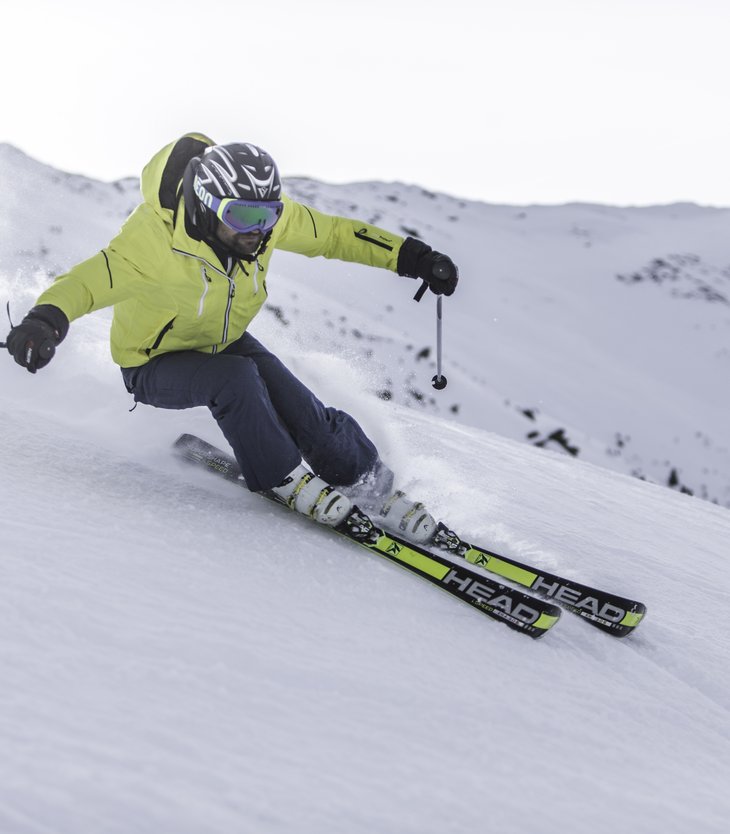 Uomo con giacca gialla scia su pendio innevato