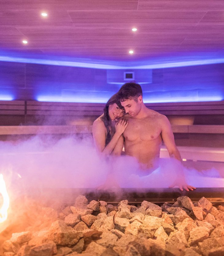 Couple relaxing in steamy sauna with stones and fire