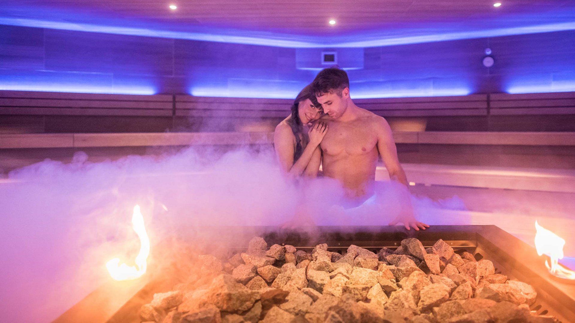 Couple relaxing in steamy sauna with stones and fire