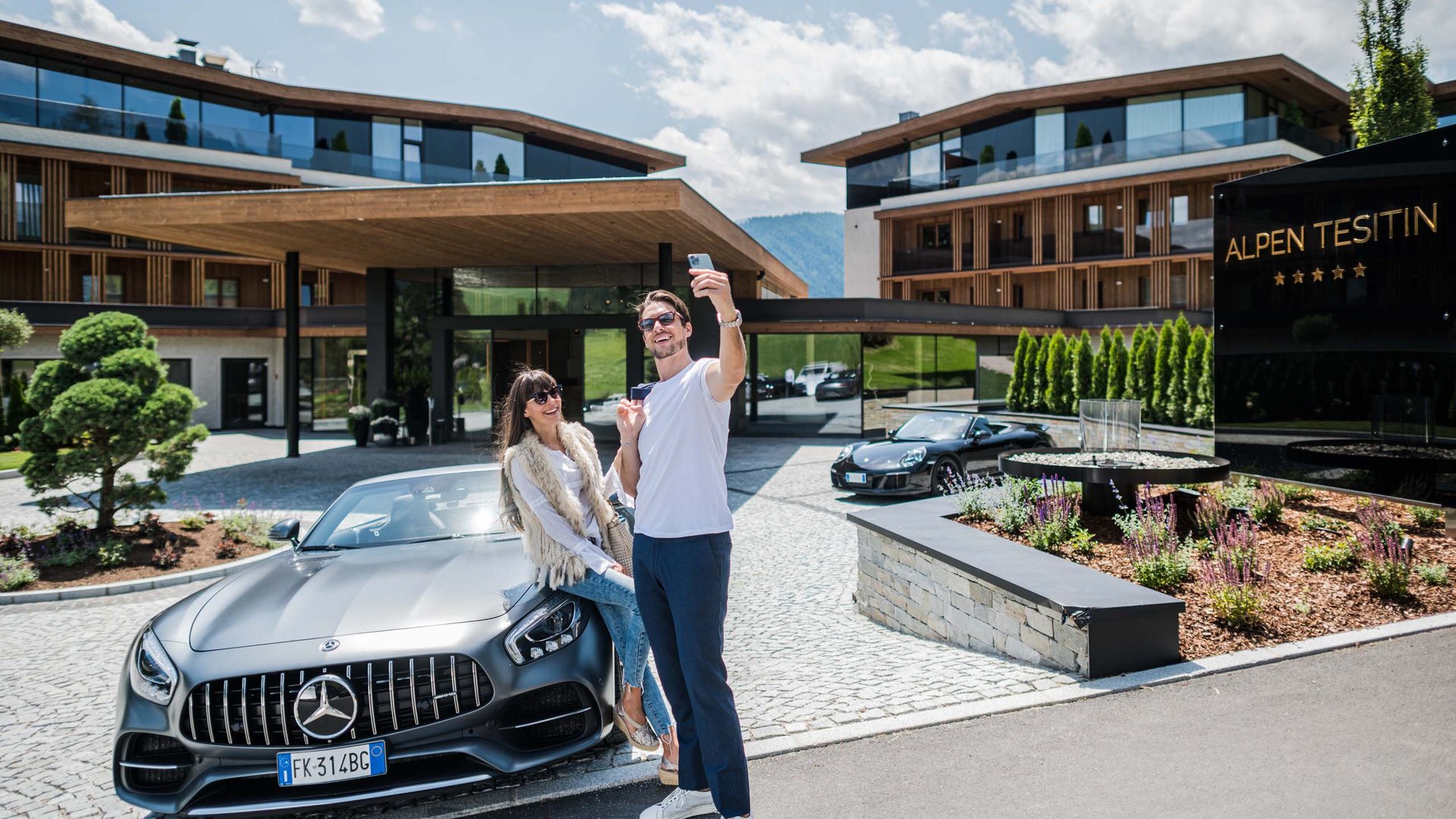 Car rental in Val Pusteria/Pustertal, Dolomites Couple taking selfie by a Mercedes convertible outside Alpen Tesitin Hotel.