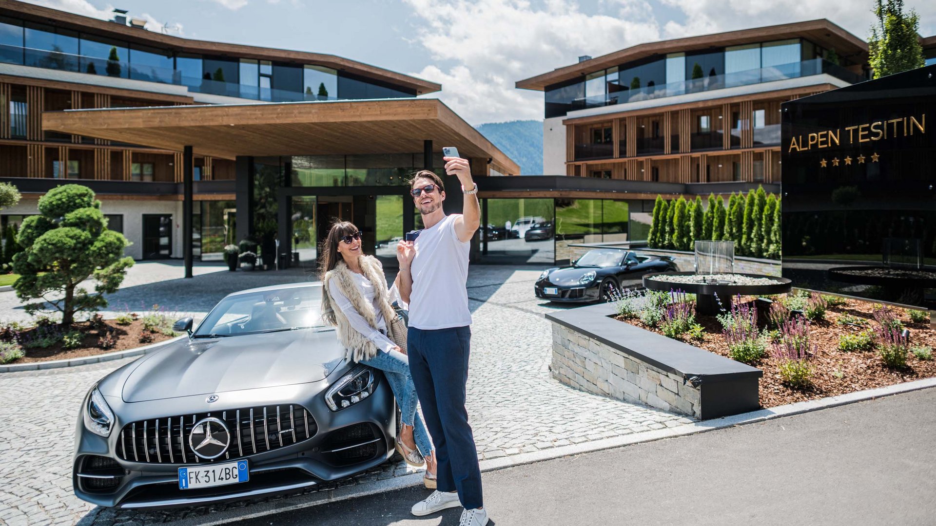 Rent a sports car in South Tyrol Couple taking selfie by a Mercedes convertible outside Alpen Tesitin Hotel.