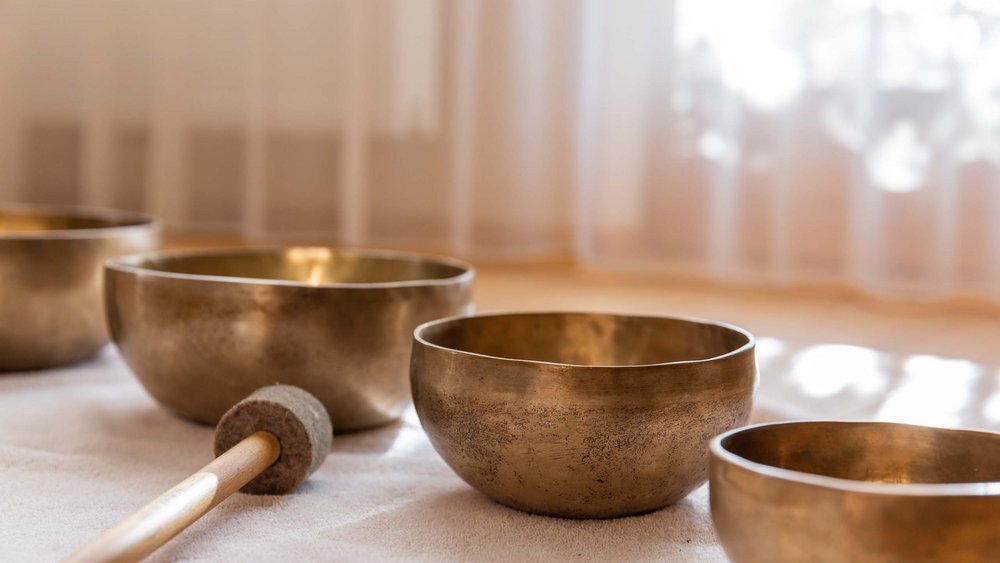 Several Tibetan singing bowls on light fabric with a wooden mallet