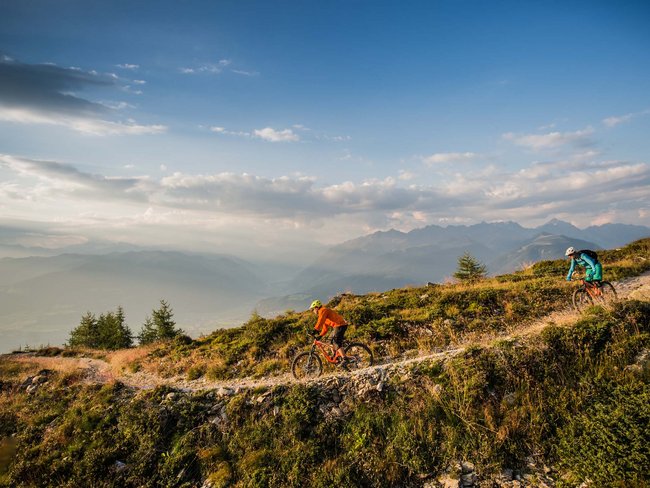 Zwei Mountainbiker fahren auf einem Bergpfad mit Alpenblick im Hintergrund